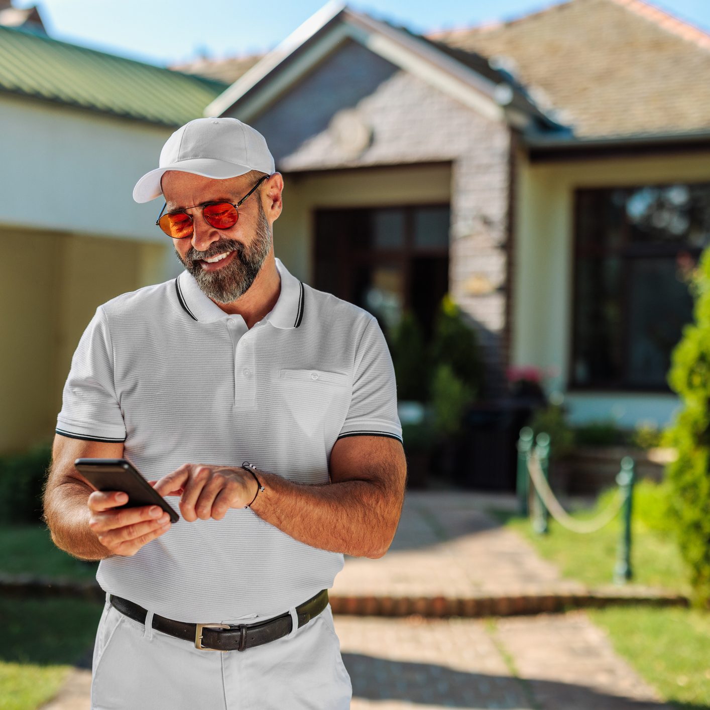 Fashionable male gold player looking happy and smiling while standing outside his house and texting